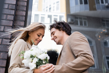 low angle view of pleased blonde woman holding white flowers near smiling man outdoors.