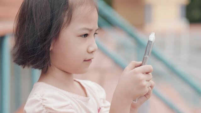 Close up face of adorable asian girl who is using smartphone alone at school which is digital lifestyle of the kid to use technology for her communication, learning and entertainment with happiness. 