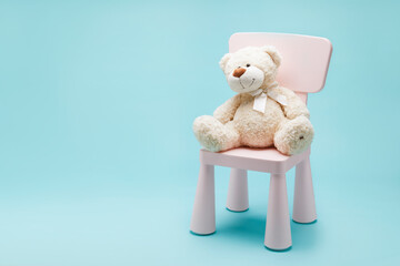 Toy bear sit on small pink chair for kids isolated on blue background.