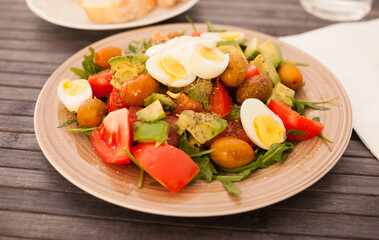 dish of fresh vegetables arugula, avocado, cherry tomatoes with olives and quail eggs on dining table