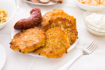 Fried grated potato pancakes with fried sausage on white plate