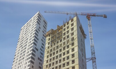 Construction site. A construction crane and a building under construction against a blue sky background. A construction crane is working, the walls of buildings are being erected.