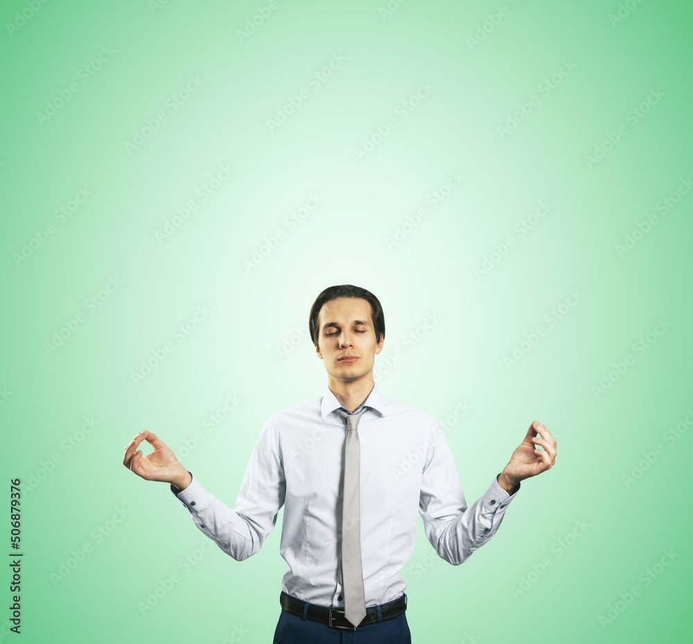 Poster calm down concept with man in white shirt in a zen pose isolated on light green wall background with