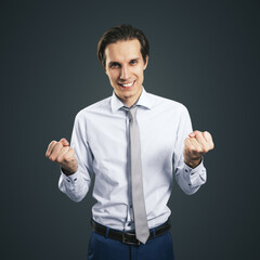 Winner and success concept with young happy man with clenched fists isolated on dark grey background