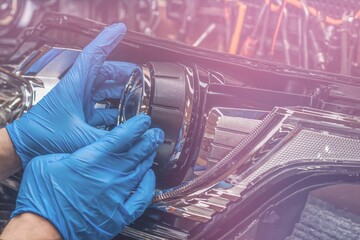 Car headlight in repair close-up. An auto mechanic wearing gloves installs the lens into the...