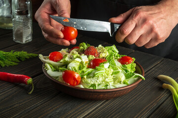 Chef prepares a vegetable salad in the kitchen table. Cutting a fresh tomato for a vitamin salad with a knife