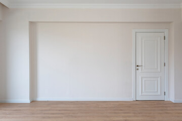 Empty room in flat flat with champagne color walls and wooden floor, white wooden door on the right side of the wall.