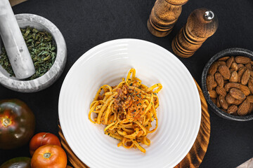 Homemade bolognese noodles with bacon and fried tomato along with ingredients used in the recipe such as tomato and oregano, with a rustic presentation of wooden plates and kitchen utensils