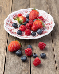 Raspberries, strawberries and blueberries on a plate over wooden table
