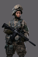 Portait of female soldier dressed in protective camouflage helmet and suit against grey background.