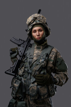 Portrait of military woman dressed in protective clothes holding rifle on her shoulder.