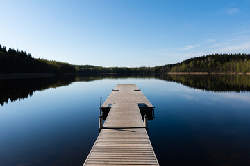 Wooden pier on a calm Lake with reflection in water on a sunny day in early summer. Merrasjärvi, Lahti, Finland.