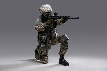 Studio shot of militant woman dressed in protective suit aiming rifle looking away.