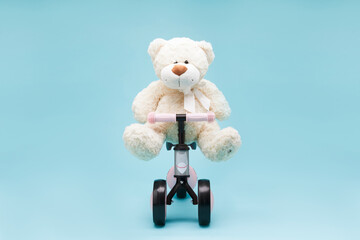Toy bear siting on modern tricycle bike for kids pedal less isolated on blue background with copy...