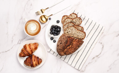 Morning breakfast setup on white surface. Flat lay of croissant, oranges, sourdough and coffee lying around.