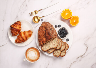 Morning breakfast setup on white surface. Flat lay of croissant, oranges, sourdough and coffee lying around.