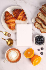 Morning breakfast setup on white surface. Flat lay of croissant, oranges, sourdough and coffee lying around.