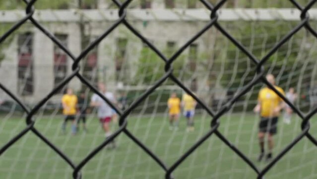 Blurred shot from behind the fence of two teams on a soccer match. Backshot of the goalkeeper 