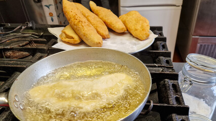 Pizza fritta napoletana ripiena di ricotta e cicoli napoletani in cottura in olio bollente in una padella d'alluminio professionale