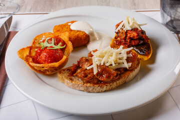 Antipasto di San Valentino di una braceria con bruschette grigliate con carne, melanzane e formaggio, polpette al sugo e frittatina di pasta con crema di formaggio