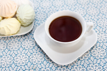 Traditional delicious brewed tea in a cup and air multicolored marshmallows lie on table with a tablecloth