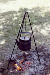Travelers warm the water in a kettle on a fire from branches in the forest. Tourist's breakfast in nature