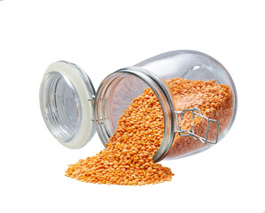 Raw red lentils spill out of a glass storage jar isolated on white background.