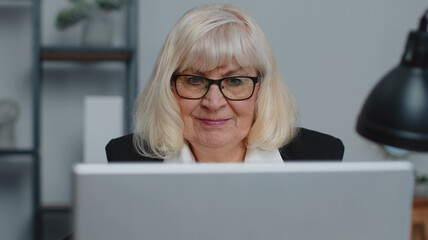 Senior mature older business woman wears glasses remote working, social distance elearning, training, online webinar at home office, using laptop computer. Close-up face elderly grandmother freelancer