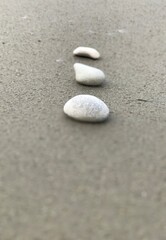 Fototapeta na wymiar Simple closeup view of vertically arranged three white stones on grey sandy beach 