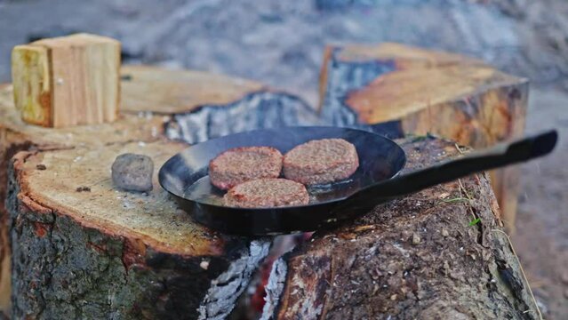 Slowly cooked and smokes three burger patties on a stainless steel frying pan in an outdoor setup. Macro close up shot of frying pan. Making food for bush craft and survival enthusiasts.