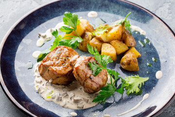 Pork neck steak served with mushroom sauce and slices of baked potatoes on a plate . The dish is decorated with bunches of parsley