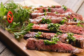 Juicy sliced beef steak with different greens and red pepper on a cutting board