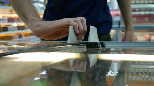 A male buyer slides the door of a refrigerator compartment and takes the frozen food package close-up