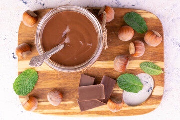 Chocolate spread or nougat cream with hazelnuts in a glass jar on a wooden board. Flat lay.
