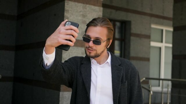 Self-loving son of businessman taking selfies on his phone outdoors. Handsome spoiled male in sunglasses taking selfie shots in different poses. Caucasian man snapping pictures of himself smiling
