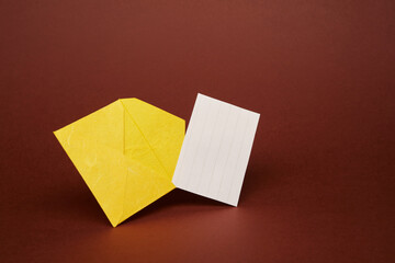 Yellow color paper office envelope with white lined sheet with copy space isolated on the bright solid fond plain dark brown background