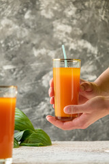 pumpkin juice with orange, hold a glass of juice in hand, human hand, two glasses with juice on a concrete table, rays of the sun, creative photo of a drink for a magazine, space for text
