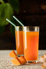 pumpkin juice with orange, orange juice in a glass with a straw, vegetable fresh in a transparent glass, two glasses with juice on a concrete table, sun rays, creative photo of a drink for a magazine,