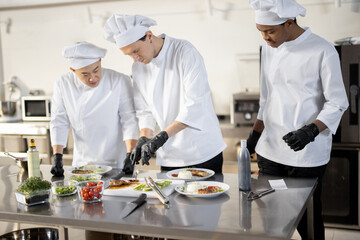 Multiracial group of cooks finishing main courses while working together in the kitchen. Asian,...