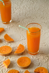 pumpkin juice with orange, pouring juice into a glass, human hand, two glasses with juice on a concrete table, sun rays, creative photo of a drink for a magazine, space for text