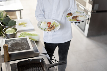 Chef holding three plates with ready meals, carrying them on hands. Cropped view without face, close-up. Concept of serving food for restaurant and haute cuisine