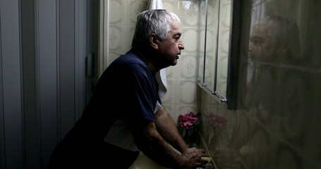Troubled senior leaning head on bathroom mirror in despair and loneliness
