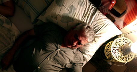 Obraz na płótnie Canvas sleepless Older man suffering from insomnia turning light on