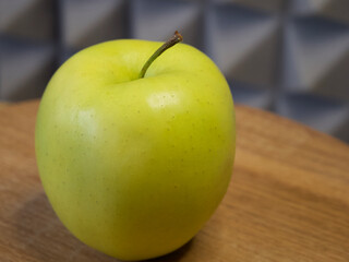 Golden Delicious is a yellow apple, one of the 15 most popular cultivars in the United States. A single apple on a wooden surface, close-up.
