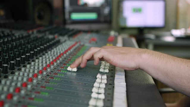 Music studio producer mixing on a console. The man is pushing up a fader on the sound mixer