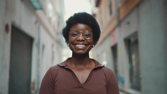 Cheerful African woman in glasses looking happy outdoors. Carefree dark-skinned girl looking at camera sincerely smiling on the street