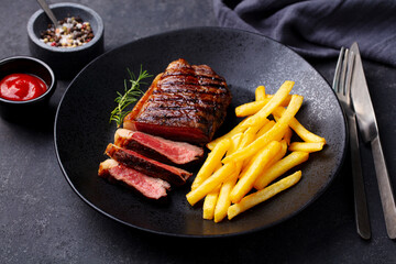 Beef Steak medium rare with French fries on a black plate. Dark background. Close up.