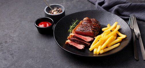 Beef Steak medium rare with French fries on a black plate. Grey background. Close up. Copy space.