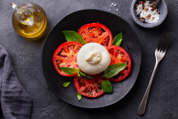 Caprese salad with tomatoes, burrata cheese and basil. Grey background. Close up. Top view.
