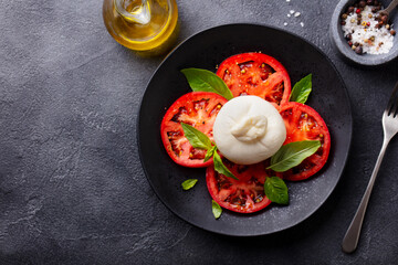 Caprese salad with tomatoes, mozzarella, burrata cheese and basil. Grey background. Copy space. Top view.